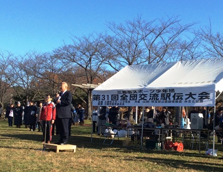 「第31回全団交流駅伝大会」と書かれた横断幕が貼られたテントの前で、小さな台の上に乗って挨拶を行っている市長の写真
