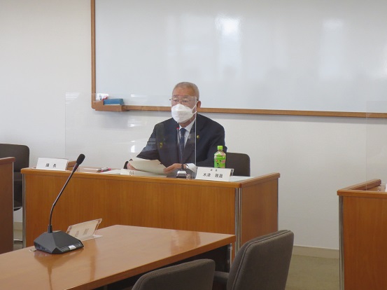 前方にホワイトボードが設置された会議室で、自席に座って挨拶をしている三郷市長の写真
