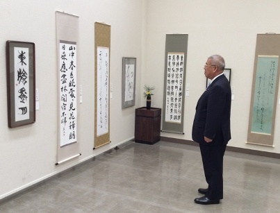 壁に掛けられた達筆な書体で書かれた作品を真っ直ぐ立ち鑑賞している市長の写真