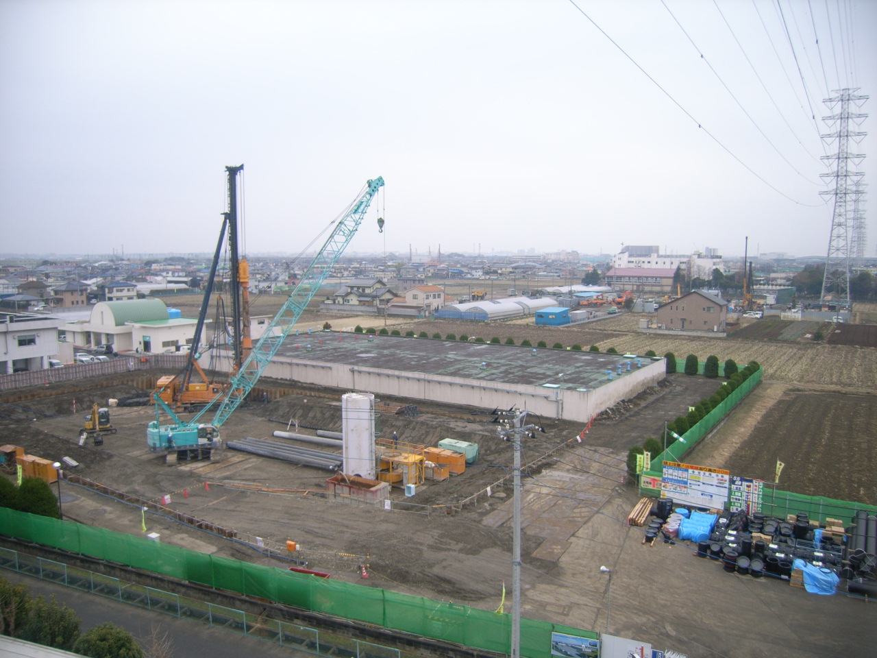 広い敷地の奥に建っている四角状の建物と、手前にクレーン車等の重機が置かれている写真
