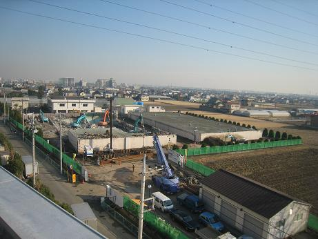 広い敷地に2つの四角状の建物が建っており、左側の建物を重機で取り壊している写真