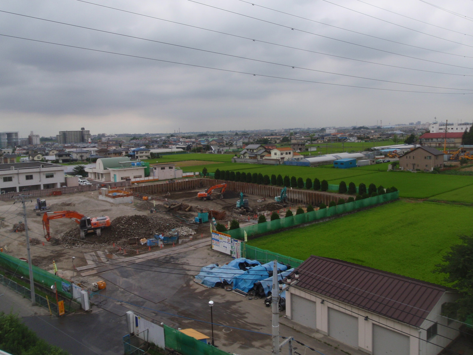 工事用フェンスで囲まれた敷地で、オレンジと緑のショベルカーが作業をしている写真