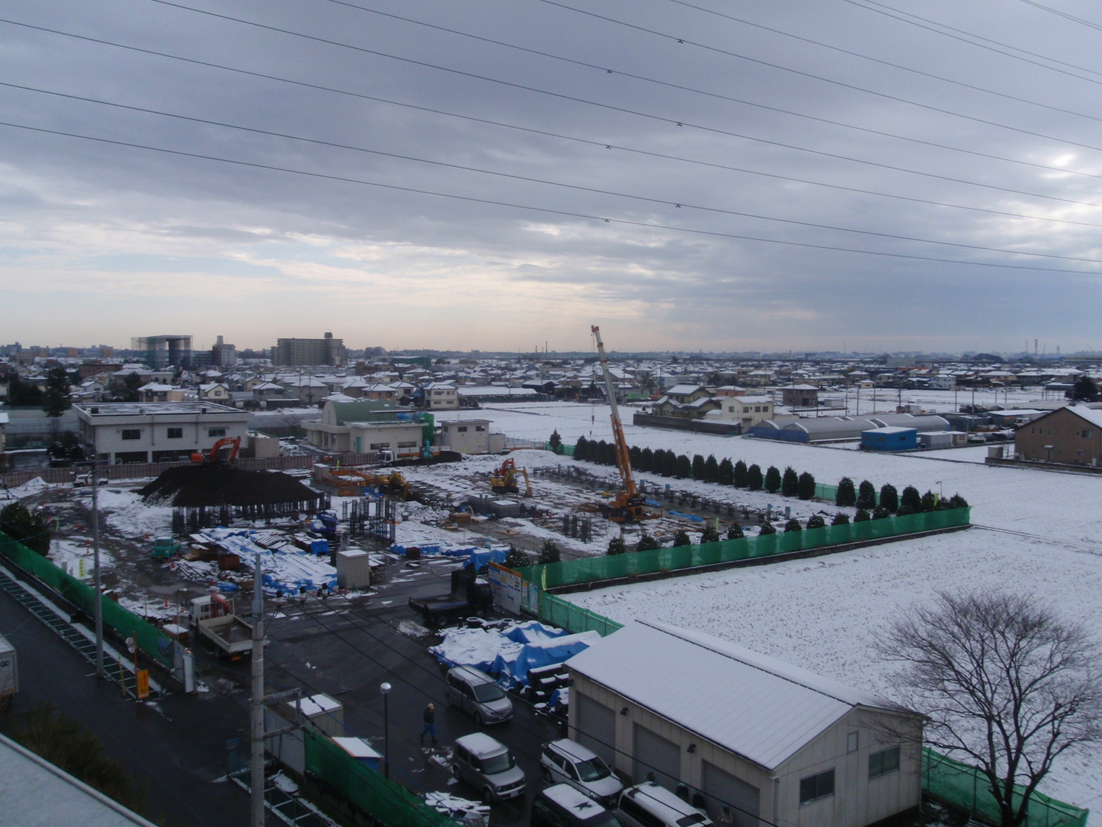 雪が積もる中、敷地内で様々な重機を使って作業をしている工事現場の写真