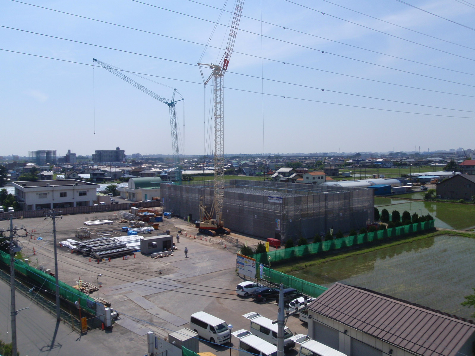 工事用フェンスで囲まれた敷地の右半分のスペースに足場が組まれており、建物を建てている様子の写真
