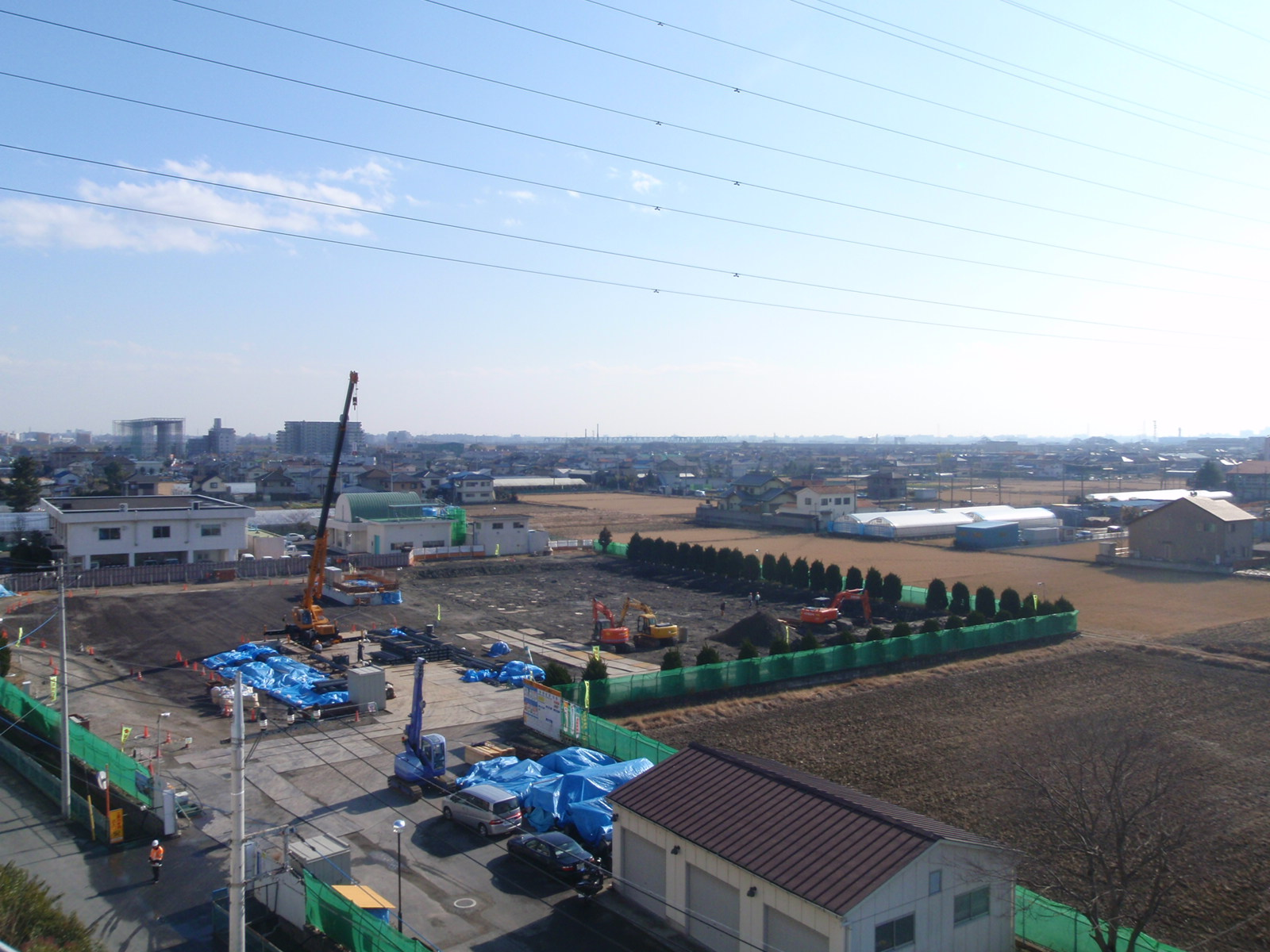 工事用フェンスで囲まれた敷地の一部分にビニールシートが敷かれ、周りでクレーン車やショベルカーが作業をしている写真
