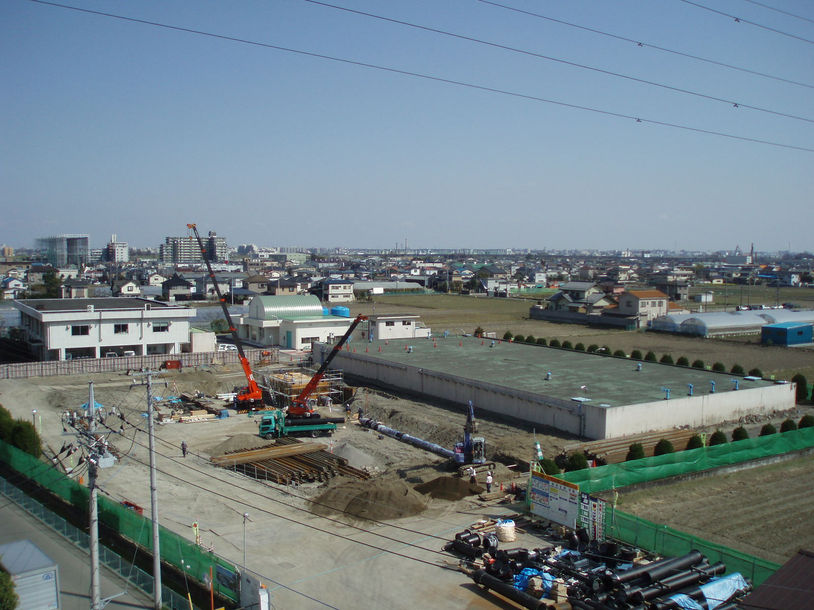 広い敷地の奥に建っている四角状の建物と、手前にクレーン車等の重機が置かれて作業をしている写真