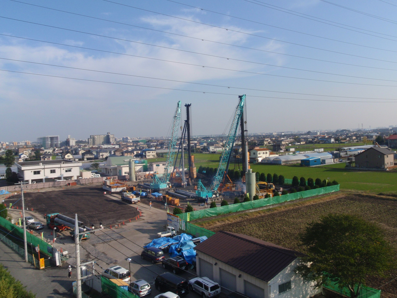 工事用フェンスで囲まれた敷地に多くの重機やトラックが並び工事をしている写真