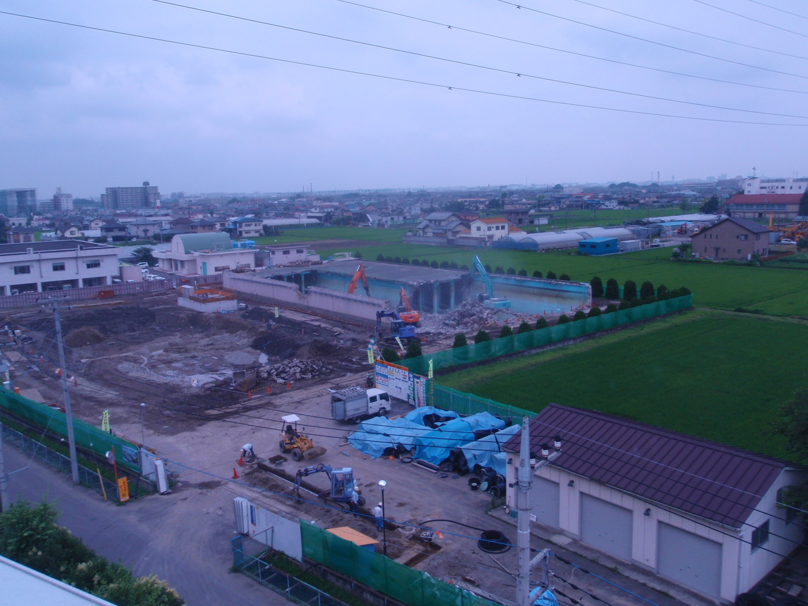 工事用フェンスで囲まれた敷地で、奥に建っている建物を重機で取り壊している写真