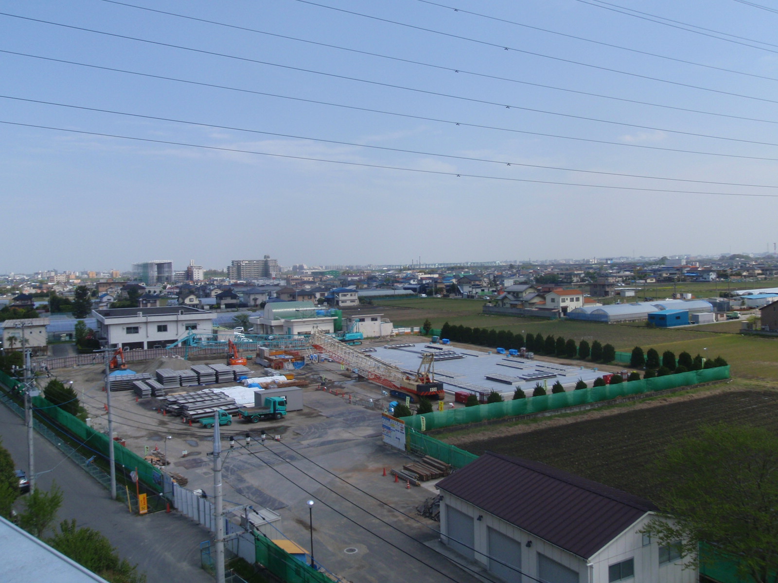 多くの工事用材料が置かれた敷地でショベルカーやトラックが様々な場所で作業をしている写真