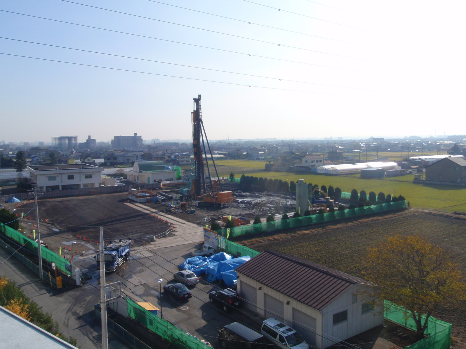 工事用フェンスで囲まれた敷地で、オレンジ色の巨大な重機が中央付近で作業をしている写真