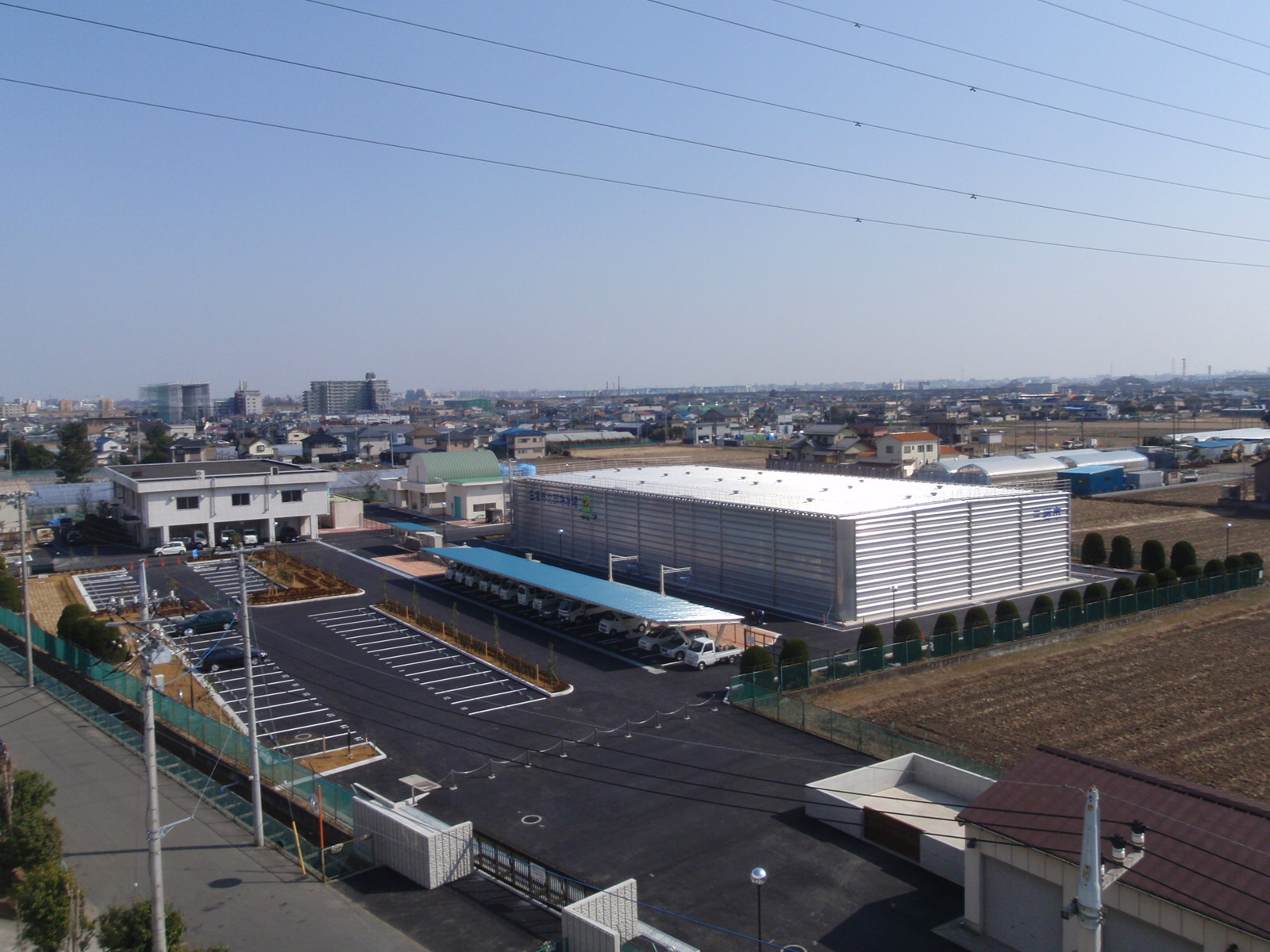 四角いステンレス製配水池の建物があり、左半分は整備された広い駐車場のある完成した配水池を撮影した写真