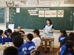 小学校の教室で、2人の栄養教諭が絵のカードを持ち説明している写真。