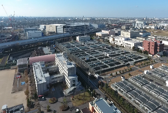 令和3年(2021年)に上空から撮影された、大きな工場やマンションが立ち並ぶ中、奥の方で大きなクレーン車が工事をしているインターチェンジ方面の写真