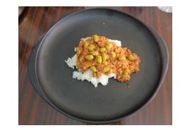 黒い丸皿の中央に盛り付けた白ご飯の上に、緑色の秋どり枝豆が入ったキーマカレーがかかっている写真