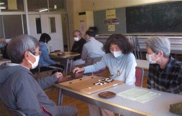 男女が対局を行い、女性の横に座る年配の方が対局を見ている様子の写真
