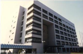 白い外壁で渡り廊下に屋根が設置された7階建ての新庁舎の外観写真