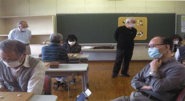 黒板に解説のためのマグネット式の碁盤が貼られ各席で対局が行われている様子の写真
