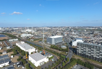 令和3年(2021年)に上空から撮影された、前方に工場、後方にマンションやオフィス、住宅が立ち並び、少し緑を残しつつも土地開発がすすんだ三郷駅方面の写真方面の写真