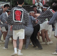 迎攝院境内でたくさんの祭礼衣装姿の男性たちが、木箱を地面にこすりつけている様子の写真