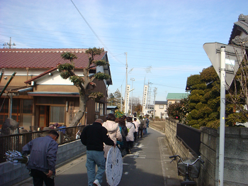 住宅街の道路を一列になって歩いている住民の方々や、オビシャの鬼が描かれた白い的を持って一緒に歩いている男性の写真