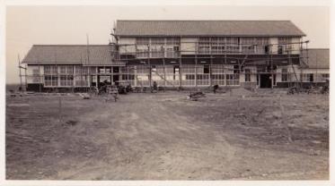 建物の周りに足場が組まれ中心部分が二階建てになっている三郷村役場外観の白黒写真