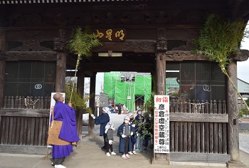 子ども達やお坊さんが笹竹の先に葉を付けたもので山門のすす払いを行っている様子の写真