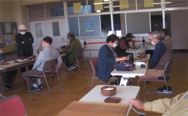 間隔をあけて机が置かれ、各席で4組ほどが悩みながら対局を行っている様子の写真