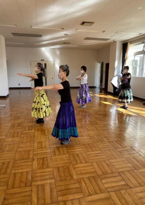 女性4名が同じ方向を向いて同じポーズをしているフラダンスの練習風景を部屋の左側から写した写真