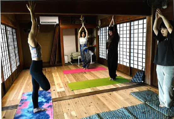 ヨガマットの上で、窓側を向き、右足は前、左足は後ろで両手を上に上げてポーズを取っている3名の女性の写真