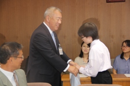 参加者が見守る中、木津市長と両手で握手を交わす発表者の男子児童の写真