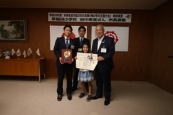 真ん中に田中希実さんが賞状を持って立ち、左隣の男性が盾をもち、市長や関係者など3名の人と記念撮影をしている写真