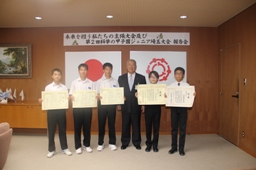 国旗と市章が飾られた市長室で、中央に木津市長、両脇に5名の男子児童達が賞状を両手で持っている様子の写真
