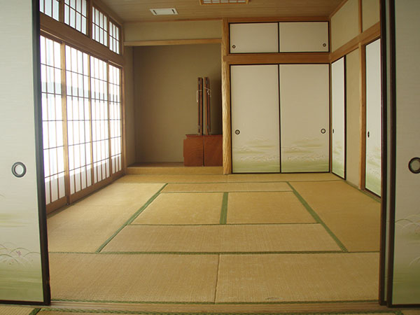 障子張りの窓と、複数のふすまの扉に囲まれた、床の間のある12畳の和室の写真