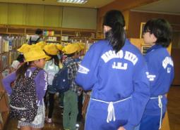 司書の方に誘導され図書館内を見学している黄色の帽子姿の子ども達を後ろから写した写真