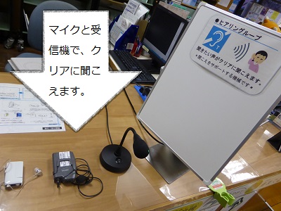 「マイクと受信機で、クリアに聞こえます。」と書かれた白矢印がテーブルの上に置かれたヒアリングループを指している写真