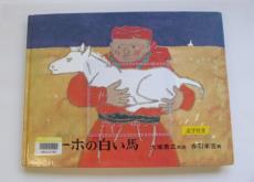 赤い民族衣装を身に着けた人物が白い馬を抱えているイラストが入っているスーホの白い馬の絵本が台の上に置かれている写真