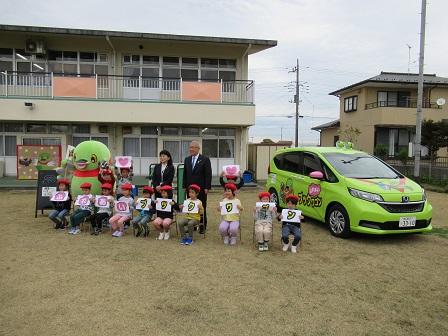 保育所の敷地内に黄緑色のふれあいブックワゴンが停まっており、市長や教育長と一緒に記念撮影をしている子ども達の写真