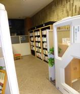 施設内通路に白い枠の装置が両側に設置され、奥に早稲田図書館予約棚が見えている写真