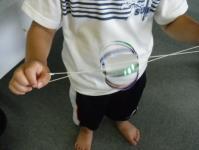 Tシャツ姿の子どもが、球体状で両側にひもが取り付けられたぶんぶんゴマを両手で引っ張っている様子の写真