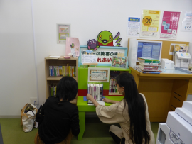 ふれあいブックサポーターが緑色の小さな本棚に本を置いている写真