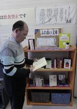 本棚の横でふれあい文庫の本を読んでいる男性を横から写した写真