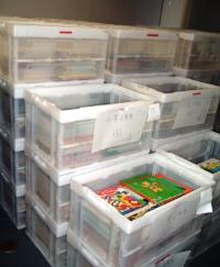多くの図書が入ったクリアボックスに張り紙が付けられ、用途ごとに分かれて積まれている写真