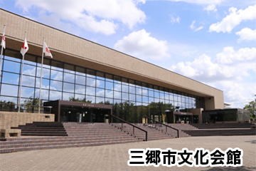 青空の下で撮影された、ガラス張りの壁を持つ文化会館正面の写真