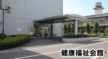 白いタイル張りの建物の、道路に面したところにある広い自動ドア前に、雨除け付きの降車スペースが設けられた健康福祉会館正面入り口の写真