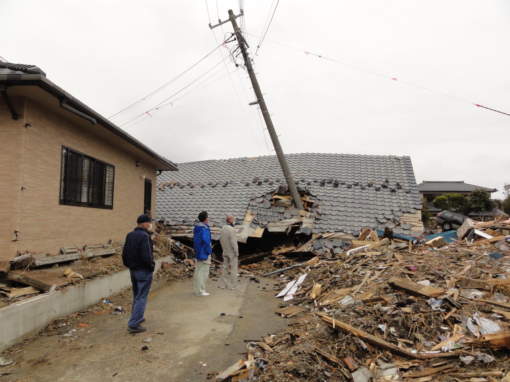 建物や電柱が倒れ、がれきが積まれている、広野町の災害現場職員視察の様子の写真