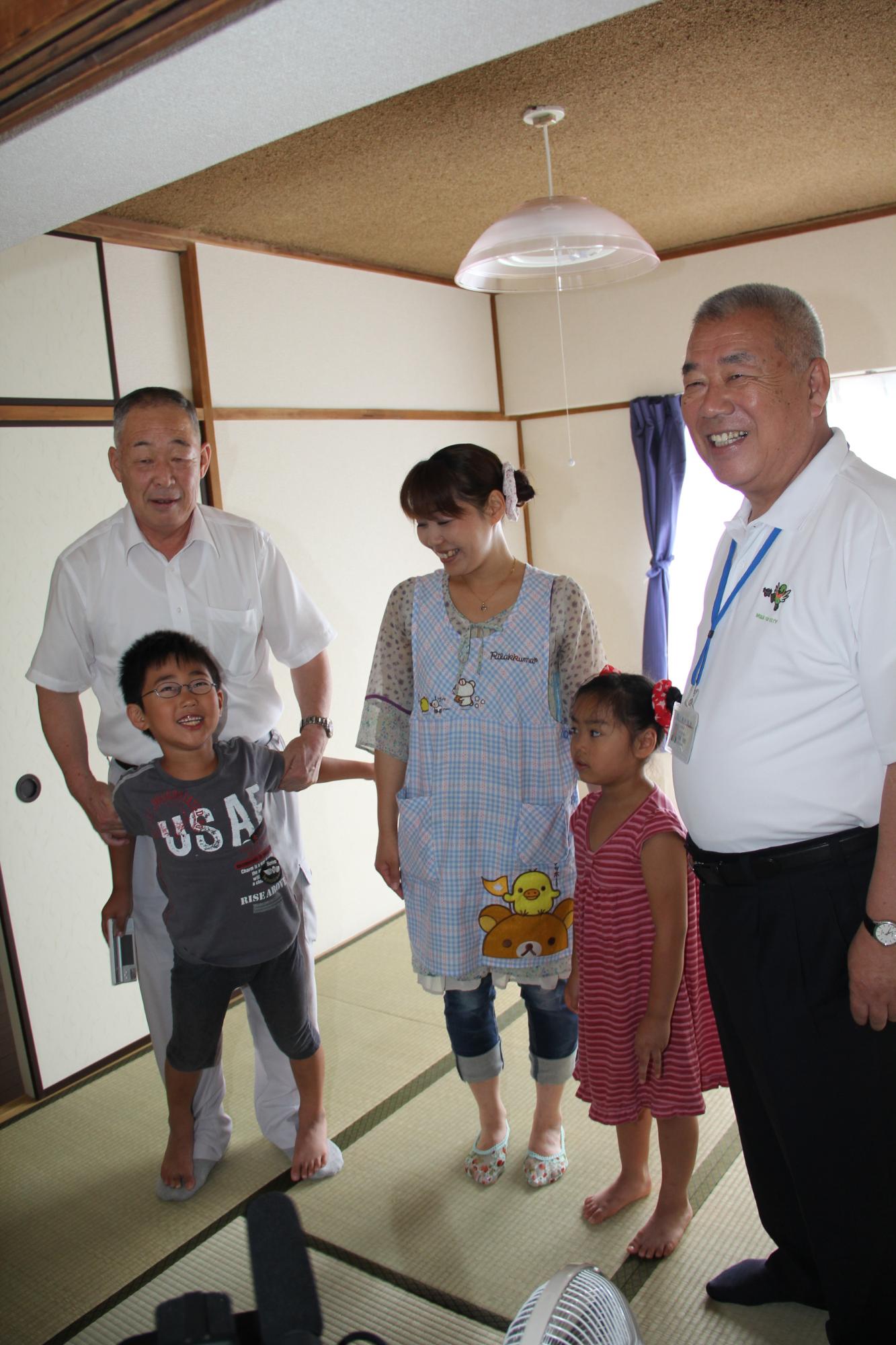 転居先の室内に立つ、笑顔の木津市長と転居された家族の写真