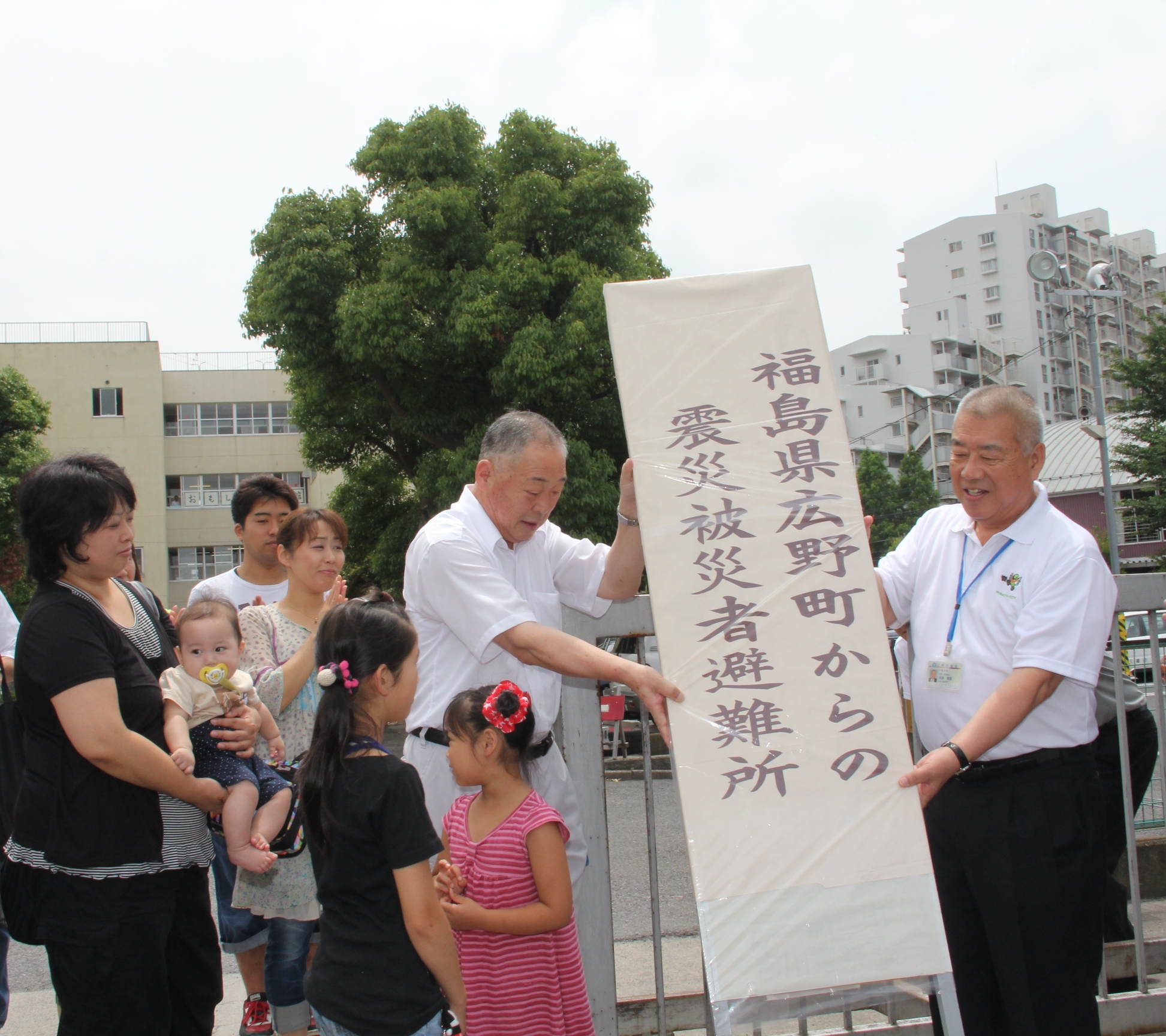 山田町長と木津市長が「福島県広野町からの震災被災者避難所」と書かれた、避難所の看板を取り外す様子とそれを見ている方々の写真