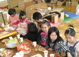 子ども達がテーブルに並べられたお菓子を囲み、小さな椅子に座りお菓子を食べている写真