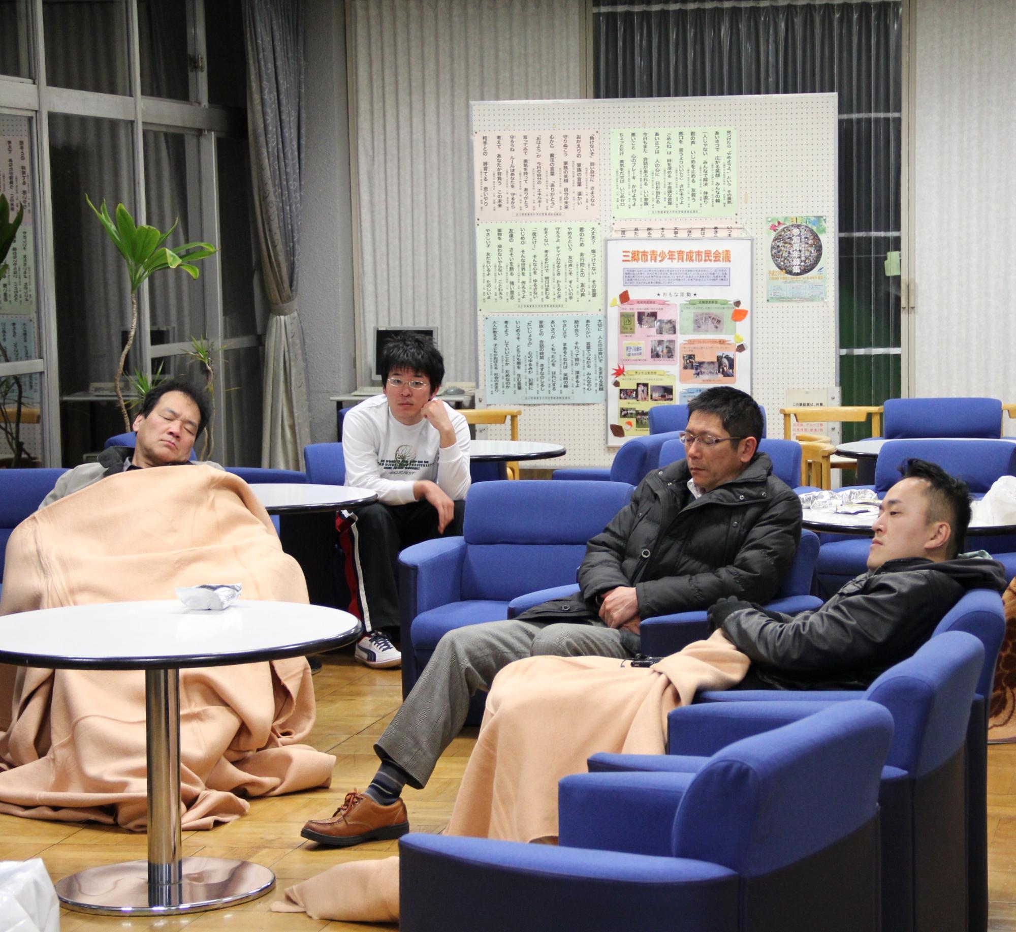 余震に対する不安を抱く方や帰宅困難者が避難所のソファに座り眠っている様子の写真