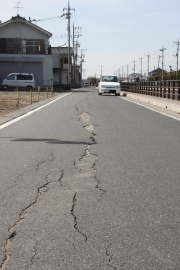 亀裂の入った市内の道路を車が走っている写真